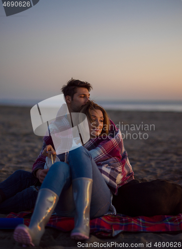 Image of Loving Young Couple Sitting On The Beach beside Campfire drinkin