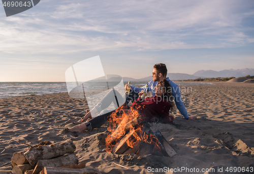 Image of Young Couple Sitting On The Beach beside Campfire drinking beer