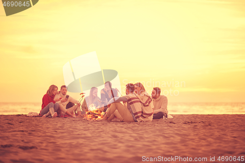 Image of Group Of Young Friends Sitting By The Fire at beach