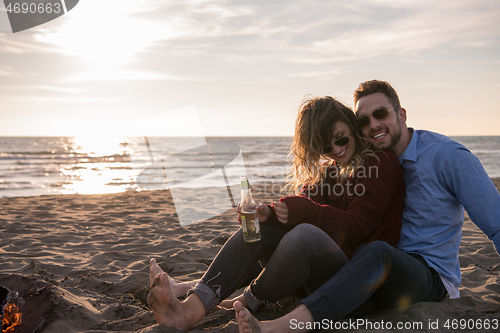 Image of Young Couple Sitting On The Beach beside Campfire drinking beer