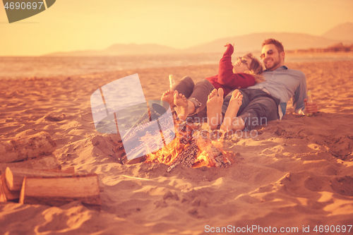 Image of Young Couple Sitting On The Beach beside Campfire drinking beer