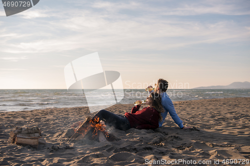 Image of Young Couple Sitting On The Beach beside Campfire drinking beer