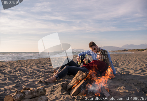 Image of Young Couple Sitting On The Beach beside Campfire drinking beer