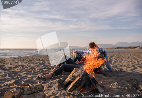 Image of Young Couple Sitting On The Beach beside Campfire drinking beer