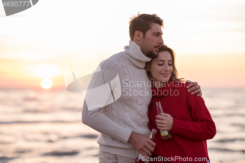 Image of Couple hugging and drinking beer together at the beach