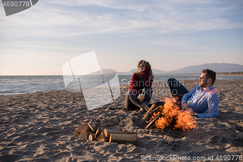 Image of Young Couple Sitting On The Beach beside Campfire drinking beer