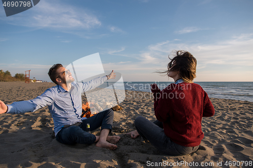 Image of Young Couple Sitting On The Beach beside Campfire drinking beer