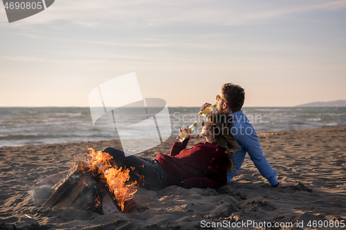 Image of Young Couple Sitting On The Beach beside Campfire drinking beer