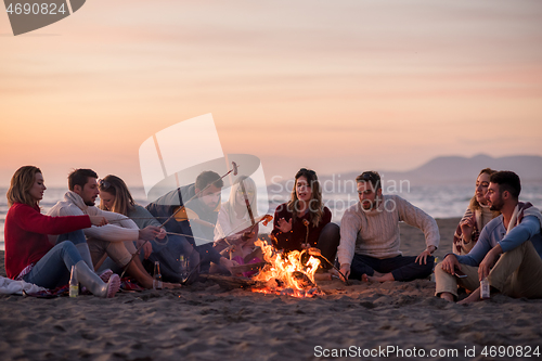 Image of Group Of Young Friends Sitting By The Fire at beach