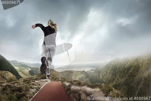 Image of Young woman running and jumping near mountains and lake