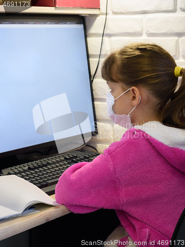 Image of A girl in a medical mask sits at a computer and learns online