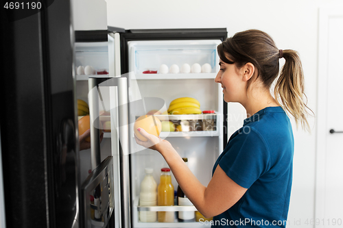 Image of happy woman taking food from fridge at home