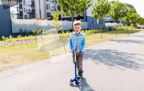 Image of happy little boy riding scooter in city