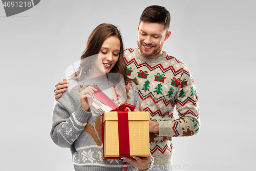 Image of happy couple in christmas sweaters with gift box