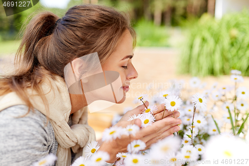 Image of happy woman smelling chamomile flowers in garden