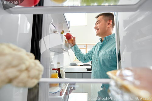 Image of man taking apple from fridge at home kitchen