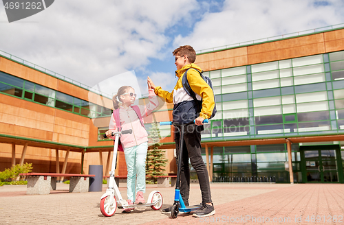 Image of happy school children with backpacks and scooters