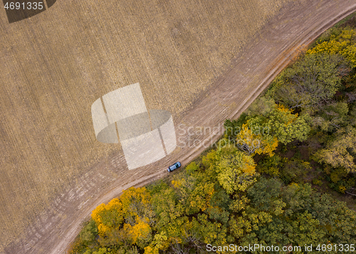 Image of Aerial view from a drone above dirt road across the agricultural field and forest area.