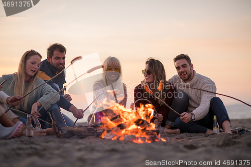 Image of Group Of Young Friends Sitting By The Fire at beach