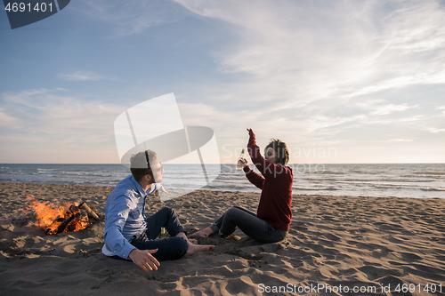 Image of Young Couple Sitting On The Beach beside Campfire drinking beer