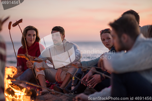 Image of Group Of Young Friends Sitting By The Fire at beach