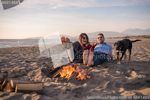 Image of Young Couple Sitting On The Beach beside Campfire drinking beer