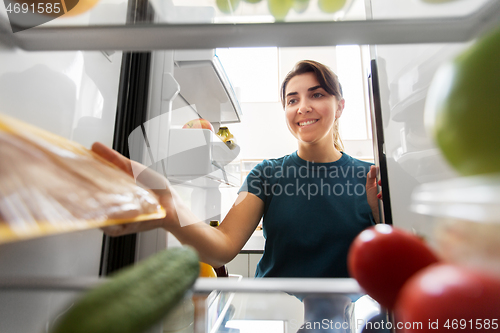 Image of happy woman taking food from fridge at home