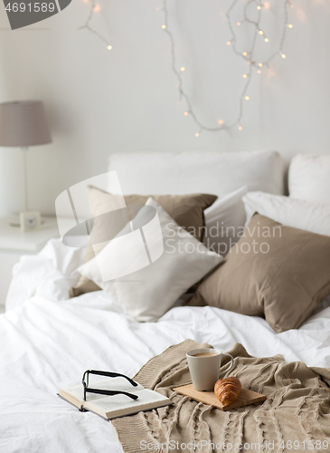 Image of coffee, croissant, blanket and book on bed at home