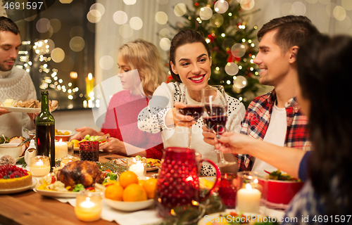 Image of happy friends drinking red wine at christmas party