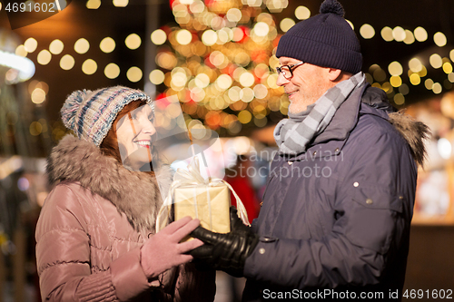 Image of happy senior couple with gift at christmas market