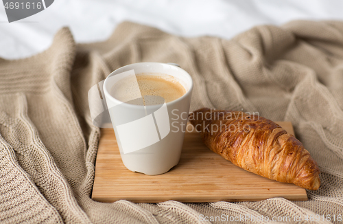 Image of cup of coffee and croissant on bed or blanket