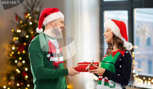 Image of happy couple in sweaters with christmas gift