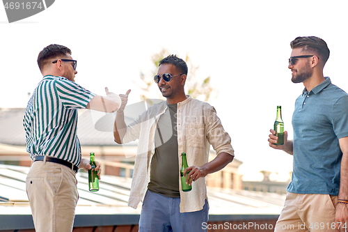 Image of happy male friends drinking beer at rooftop party