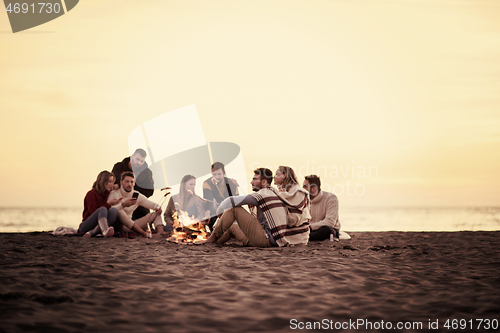 Image of Group Of Young Friends Sitting By The Fire at beach