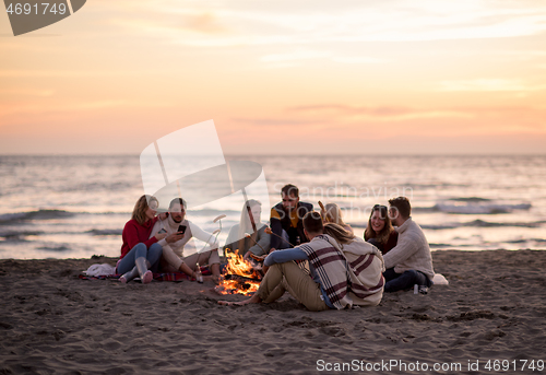 Image of Group Of Young Friends Sitting By The Fire at beach