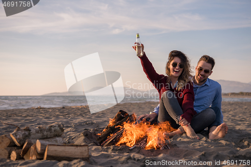 Image of Young Couple Sitting On The Beach beside Campfire drinking beer