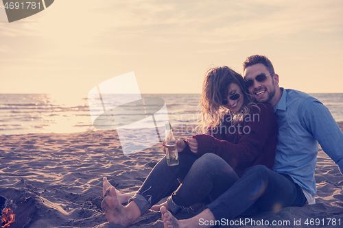 Image of Young Couple Sitting On The Beach beside Campfire drinking beer