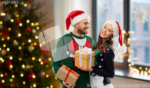 Image of happy couple in ugly sweaters with christmas gifts