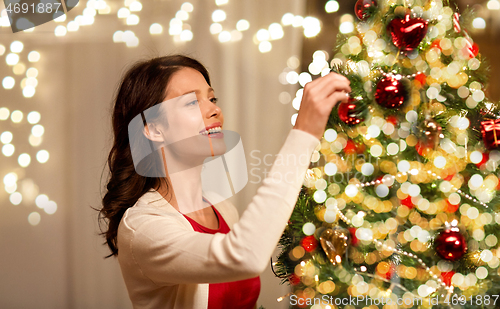 Image of happy woman decorating christmas tree at home