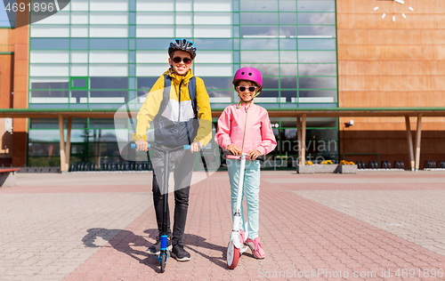 Image of happy school children in helmets riding scooters