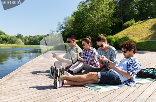 Image of friends with smartphone on lake pier in summer