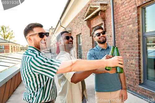 Image of happy male friends drinking beer at rooftop party