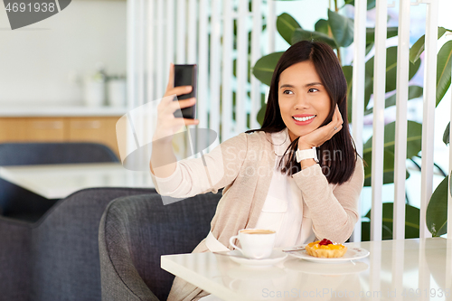 Image of asian woman taking selfie by smartphone at cafe