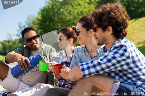 Image of happy friends drinking tea from thermos in summer