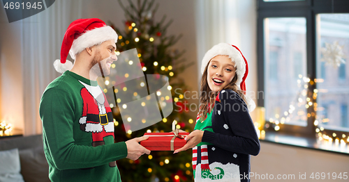 Image of happy couple in ugly sweaters with christmas gift