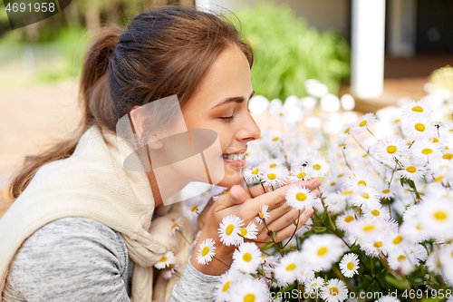 Image of happy woman smelling chamomile flowers in garden