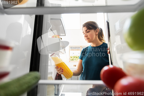 Image of woman taking bottle of juice from fridge at home