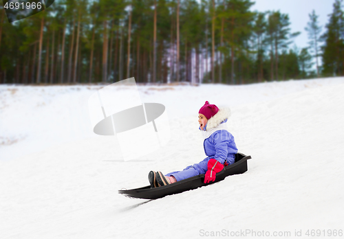 Image of happy little girl sliding down on sled in winter