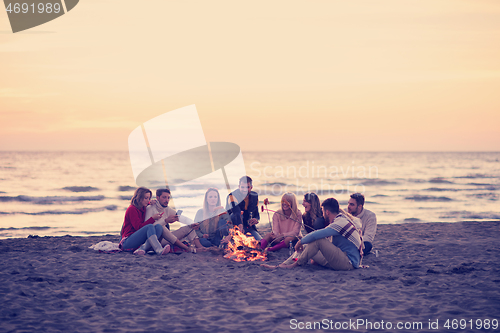 Image of Group Of Young Friends Sitting By The Fire at beach