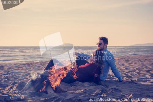 Image of Young Couple Sitting On The Beach beside Campfire drinking beer